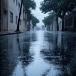 Rua brasileira sob chuva intensa, com nuvens escuras e poças d'água, ilustrando alerta laranja do Inmet para chuvas fortes em cinco estados.