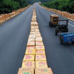 Rodovia BA-262 na Bahia bloqueada por barreiras de caixas de cacau em protesto de produtores por preços justos, com plantações ao fundo.