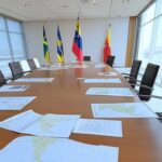Mesa de reunião com bandeiras da China e Venezuela, mapas da América do Sul, em sala diplomática em Brasília.
