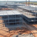Construção de fábrica de whey protein da Sooro Renner no Paraná, com estruturas industriais e guindastes em paisagem brasileira.