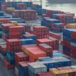 Porto brasileiro com contêineres e navio de carga, ilustrando impacto de tarifas dos EUA nas exportações do Brasil.