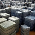 Centro de coleta de embalagens de defensivos agrícolas no Brasil, com pilhas de recipientes recicláveis em galpão rural e lavouras ao fundo.