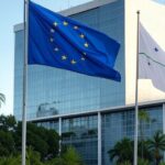Bandeiras da UE e Mercosul em edifício governamental brasileiro, representando acordo comercial e rebote a críticas europeias.