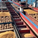 Porto brasileiro com navios cargueiros carregando exportações de grãos como soja e milho.