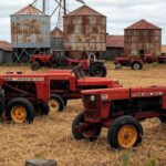 Fazenda abandonada no Brasil com silos enferrujados e campos secos, ilustrando falências agrícolas.