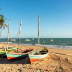 Barcos de pesca artesanal em praia brasileira, simbolizando bolsas de estudo para jovens pescadores pelo Ministério da Pesca.