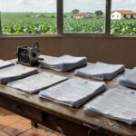 Mesa com documentos tributários em escritório rural brasileiro, ao fundo plantação de soja, representando lei complementar e Funrural.