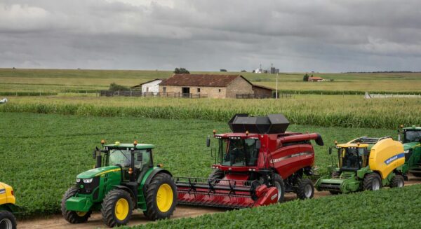 Feira agrícola Expodireto Cotrijal com estandes de máquinas e campos de cultivo sob céu nublado, debatendo clima e mercado.