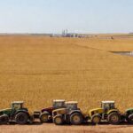 Plantação de soja no Brasil com tratores e tanques de diesel, representando debate sobre tributos no agro e biodiesel.