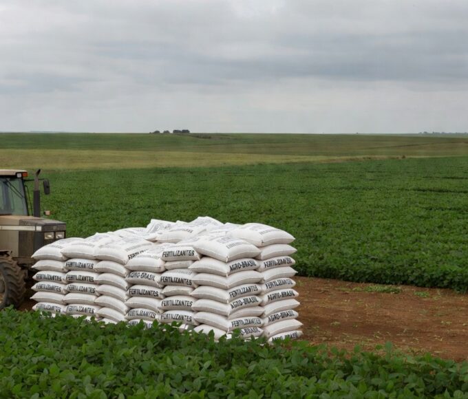 Lavoura de soja no Brasil com sacos de fertilizantes, ilustrando alerta sobre preços elevados devido à guerra no Oriente Médio.