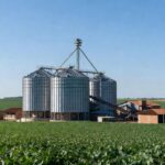 Silos de armazenagem de grãos em plantação no Brasil, destacando déficit de 130 milhões de toneladas.