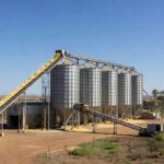 Fábrica de rações no Brasil com silos e grãos, representando crescimento na produção para 2026.
